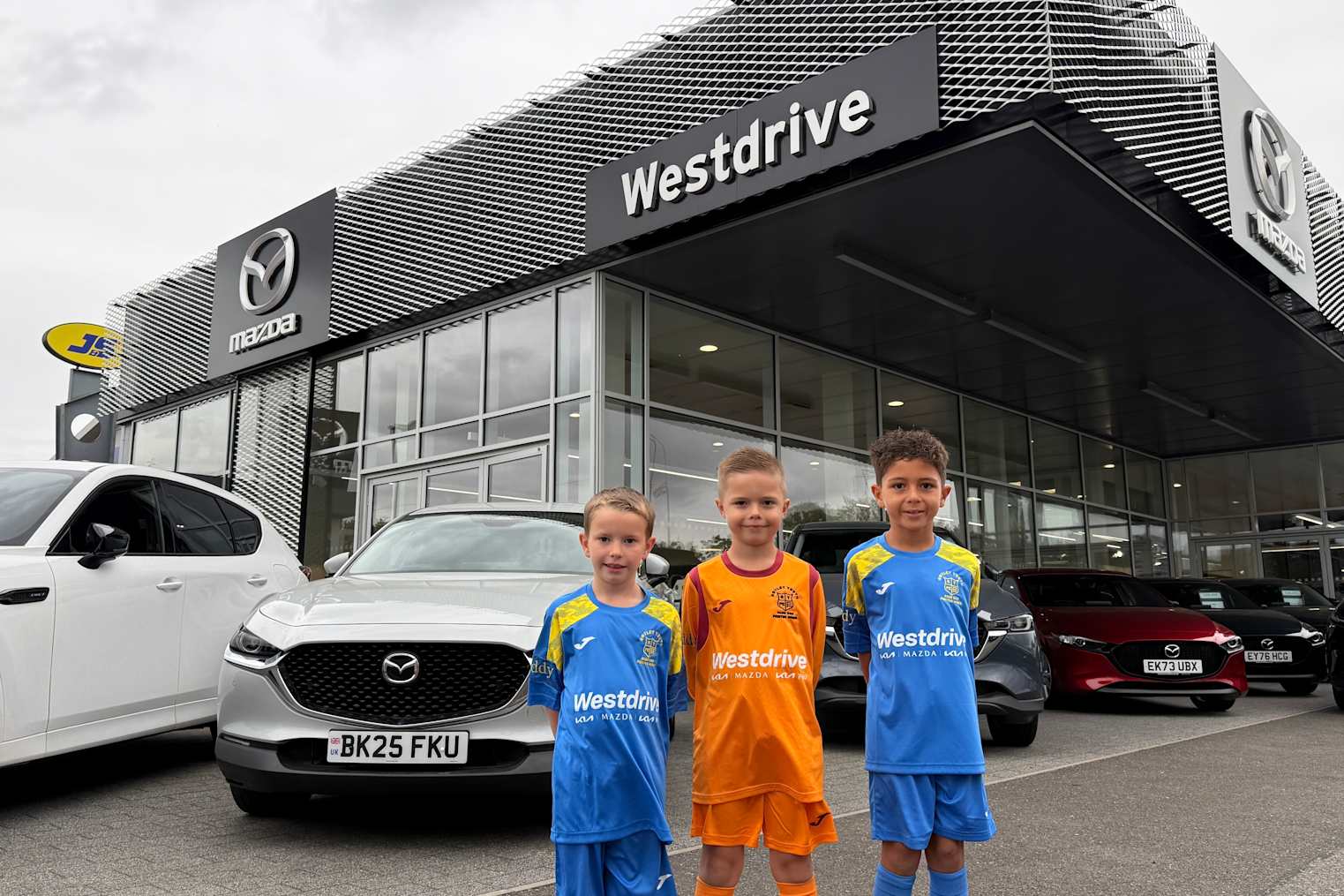Notley Youth FC Under 8s Kestrels in their new kit posing in front of Mazda cars at Westdrive Mazda Braintree