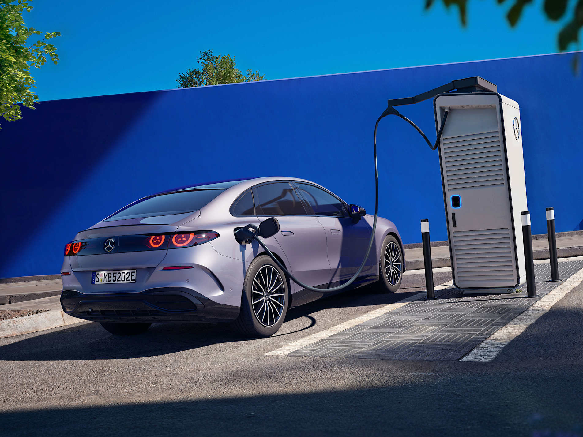 Silver electric Mercedes-Benz C-Class charging at a public station against a blue wall