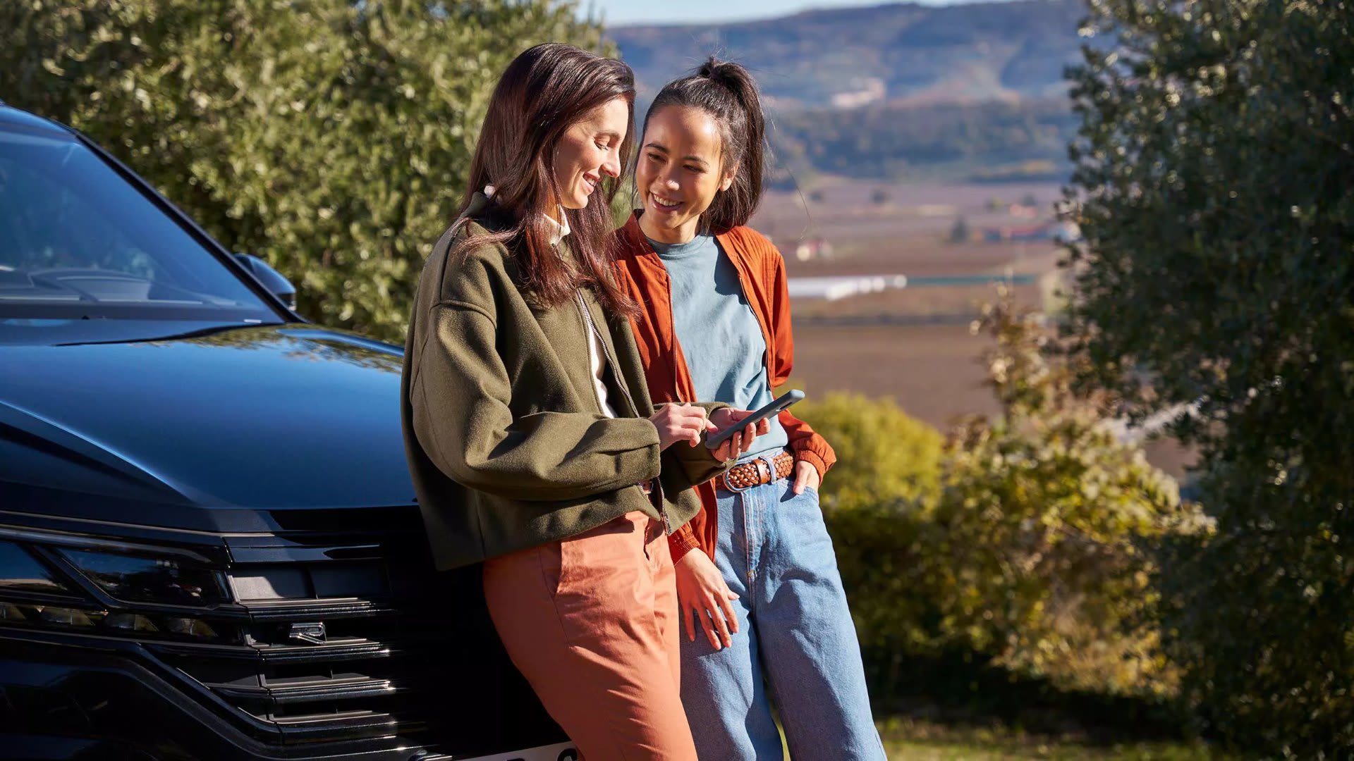 Two women talking while leaning on a Volkswagen – Volkswagen warranties explained by Camerons Volkswagen, Perth