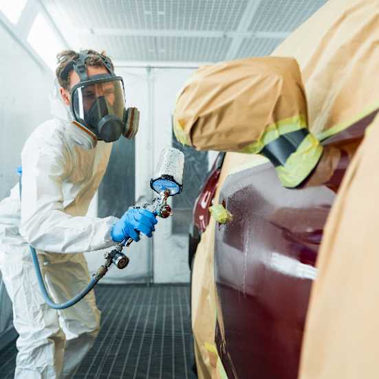 Man in a protective suit and mask restoring the car door's paint using a spray gun.