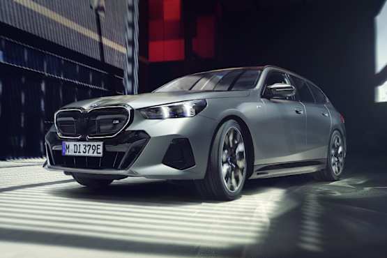 A sleek grey BMW i5 Touring M60 xDrive car parked in a modern urban setting with dramatic lighting and shadows