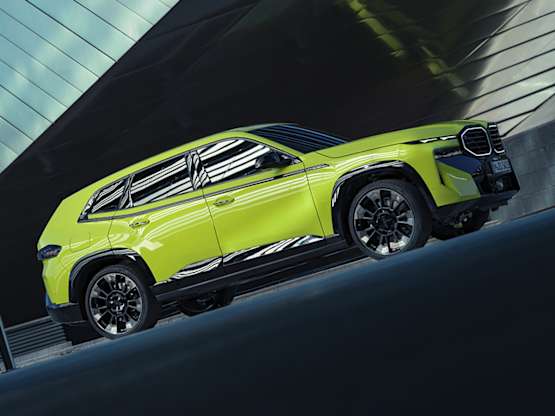 A bright yellow BMW XM parked against a modern architectural backdrop, showcasing its sleek design.