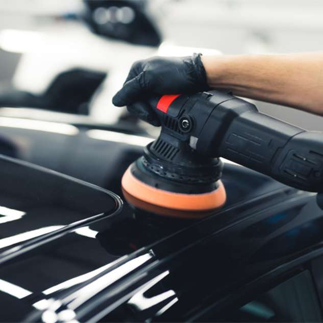 Hands of a man with a polisher in repair shop polishing black sports car