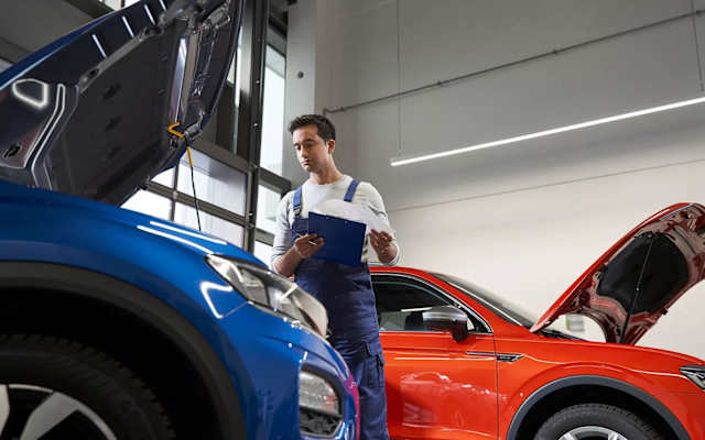 Smiling Volkswagen service manager holding paperwork with a car on a ramp behind – Camerons Volkswagen, Perth
