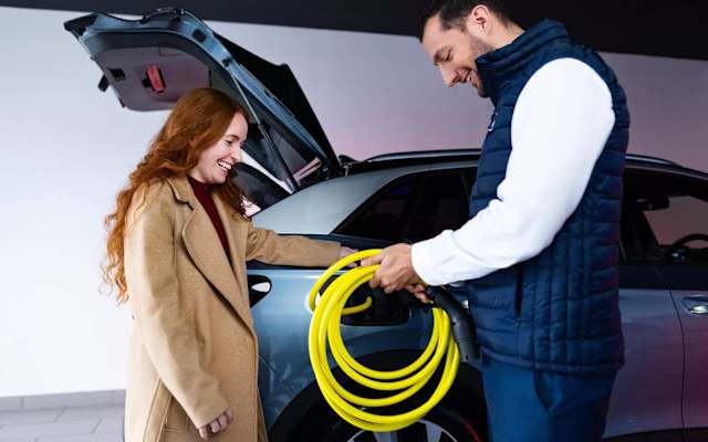 Couple beside a Volkswagen Approved Used car holding a charging cable – Approved Used offers at Camerons Volkswagen, Perth